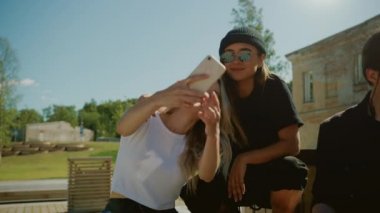 Şık Cool Gençler Park Banklar Üzerinde Chilling, Smartphone kullanarak, Selfies alarak. İki Kız ve İki Erkek Sosyal Medyada Konuşuyor ve Eğleniyor. Hip Park Şehrin Gentrified Parçası