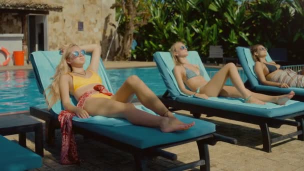 Dolly Shot of Three Beautiful Young Women Bain de soleil, allongé dans des chaises longues près de la piscine extérieure. Magnifiques filles minces en maillot de bain se bronzer sur la destination glamour et Voyage — Video