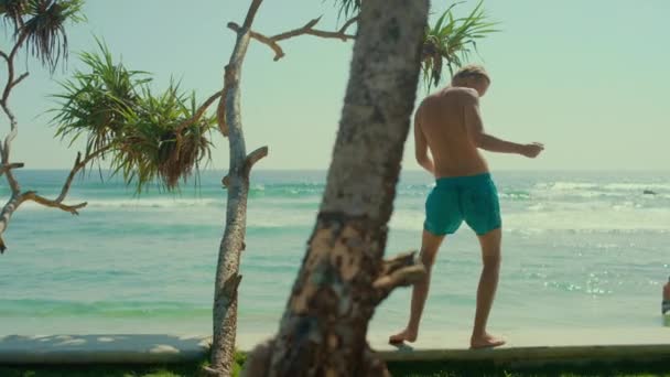 水泳ショートパンツを着たハンサムでアスレチックマンは、深いぼかしシーハーバービューで桟橋を歩きながら踊ります。ガイダンスと休暇中の楽しみを持っています。スローモーションで — ストック動画