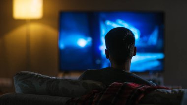 Onun büyük düz ekran televizyonda film izlerken bir kanepede oturan bir adam arkadan görünüm.