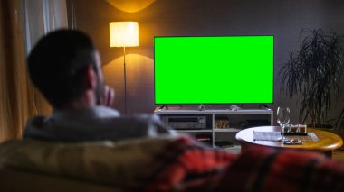 Akşam bir orta arkadan görünüm büyük düz ekran Tv izlerken kanepede oturan adam yaşlı..