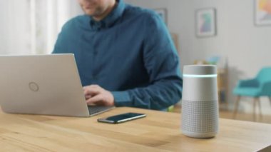 Laptop'ta Masasında Oturan Adam, Yapay Zeka Yardımı ile Akıllı Hoparlör Yanında Sorular Yanıtlar, Müzik, Podcast çalış. Hoparlör Ekolayzır Işıklar Gösterir