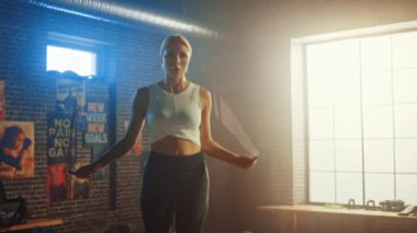 Fit Atletik Sarışın Kadın Egzersizleri Bir Loft Style Sanayi Spor Salonu'nda İp Atlama ile. O onu yoğun çapraz fitness eğitim programı yok. Tesiste Duvarda Motivasyon Posterleri bulunmaktadır. Yavaş Çekim.