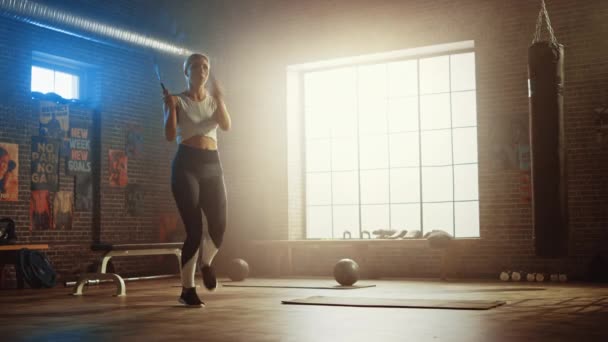 Vestibilità atletica Bionda Donna Esercizi con corda da salto in una palestra industriale stile Loft. Si è concentrata sul suo intenso programma di allenamento cross fitness. Lo strumento ha manifesti motivazionali sul muro . — Video Stock