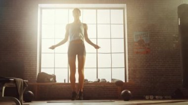 Loft Style Sanayi Spor Salonu'nda Atlama Halat ile Güçlü Atletik Kadın Egzersizleri. Yoğun Cross Fitness Eğitim Programına odaklanmış. Arkasında Büyük Pencere.