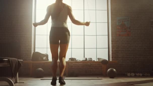 Ejercicios fuertes de la mujer atlética con la cuerda que salta en un gimnasio industrial del estilo Loft. Está concentrada en su intenso programa de entrenamiento físico. Mirando hacia la ventana grande. Disparo de espalda . — Vídeos de Stock