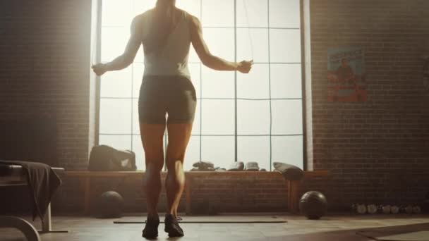 Silná atletická žena cvičení s skákací lanem ve stylu podkroví průmyslová tělocvična. Soustředí se na svůj program intenzivní Přícvik. Čelem k velkému oknu. Zadní záběr.