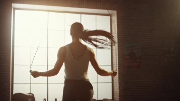 Сильная атлетическая женщина упражняется с веревкой для прыжков в лофт стиле индустриальный тренажерный зал. Она сконцентрировалась на программе интенсивной перекрестной физической подготовки. Лицом к большому окну. Back Shot . — стоковое видео