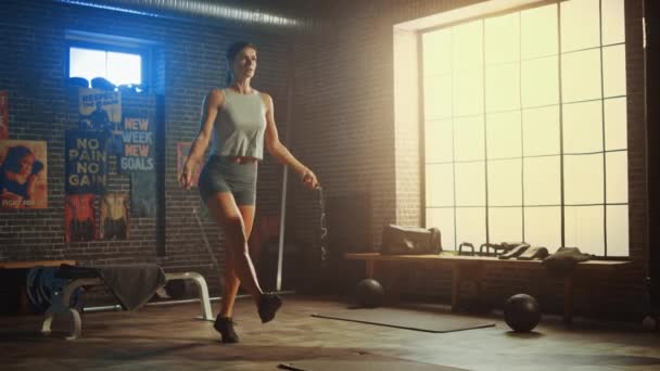 Сильная атлетическая женщина упражняется с веревкой для прыжков в лофт стиле индустриальный тренажерный зал. Она сконцентрировалась на программе интенсивной перекрестной физической подготовки. Объект имеет мотивационные плакаты на стене . — стоковое видео
