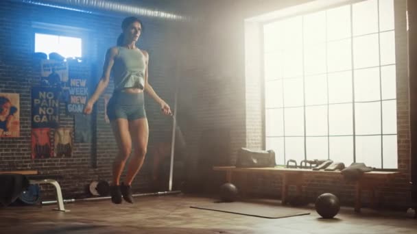 Ejercicios fuertes de la mujer atlética con la cuerda que salta en un gimnasio industrial del estilo Loft. Está concentrada en su intenso programa de entrenamiento físico. Facilidad tiene afiches motivacionales en la pared . — Vídeos de Stock