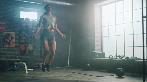 Ισχυρή αθλητική γυναίκα ασκήσεις με άλμα σχοινί σε μια σοφίτα βιομηχανικό γυμναστήριο. Είναι συγκεντρωμένη στο πρόγραμμα εντατικής γυμναστικής της. Η εγκατάσταση έχει αφίσες κινήτρων στον τοίχο. — Αρχείο Βίντεο
