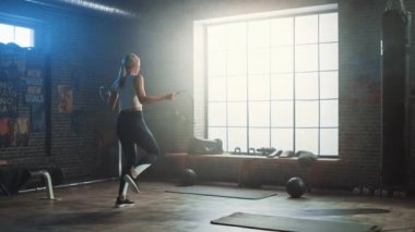 Fit Atletik Sarışın Kadın Egzersizleri Bir Loft Style Sanayi Spor Salonu'nda İp Atlama ile. Yoğun Cross Fitness Eğitim Programını Yapıyor. İpin Üzerinden Atlamak için Başarısız Olur ve Atar.