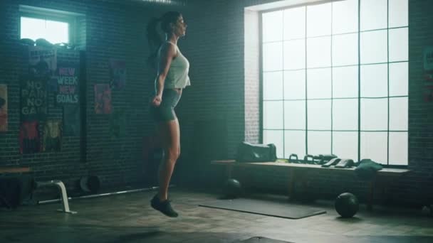 Сильная атлетическая женщина упражняется с веревкой для прыжков в лофт стиле индустриальный тренажерный зал. Она проходит интенсивную тренировку по фитнесу. Перепрыгнуть через канат . — стоковое видео