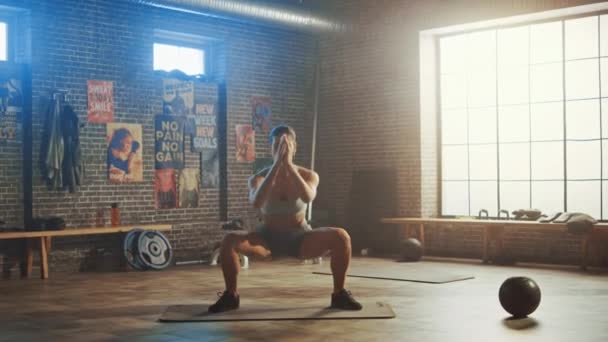 Silný a fit krásná atletická žena ve sportovní top a šortky je dělat squat cvičení v Loft stylu průmyslové tělocvičny s motivačními plakáty. Je to součást jejího tréninku Cross Fitness.. — Stock video