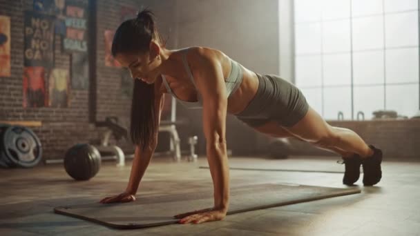 Silná a fit atletická žena ve sportu Top a šortky se účastní cvičení ve stylu podkroví průmyslová tělocvična s motivačními plakáty. Je to součást tréninkového tréninku. Teplé světlo.