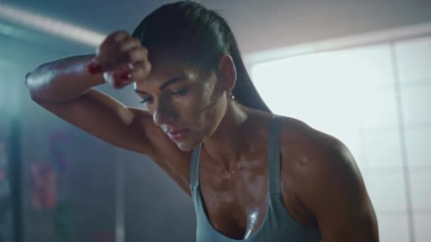 Close Up Portrait of a Beautiful Strong Fit Brunette Wiping Sweat from Her Face in a Loft Industrial Gym with Motivational Posters. Ela está a recuperar a respiração depois do treino de fitness intenso. . — Vídeo de Stock