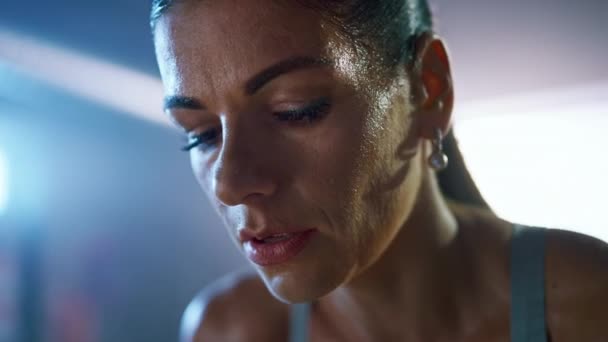 Fermer Portrait d'une belle brune bien ajustée qui essuie la sueur de son visage dans une salle de sport industrielle Loft avec des affiches motivantes. Elle reprend son souffle après un entraînement intense de remise en forme . — Video