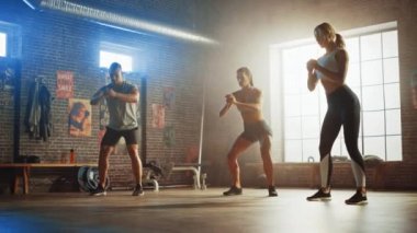 Güçlü Erkeksi Erkek ve İki Fit Atletic Kadın Squat Egzersizleri yapıyoruz. Onlar Duvarlarda Motivasyon posterleri ile bir Loft Spor Salonunda Egzersiz. Bu Sunny ve Oda Sıcak Işık vardır. Onların Takım Fitness Parçası.
