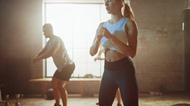 Starker männlicher Mann und zwei fitte atletische Frauen machen Kniebeuge-Übungen. Sie trainieren in einer Loft-Turnhalle mit Motivationsplakaten an den Wänden. Es ist sonnig und das Zimmer hat warmes Licht. Teil ihrer Team-Fitness. — Stockvideo