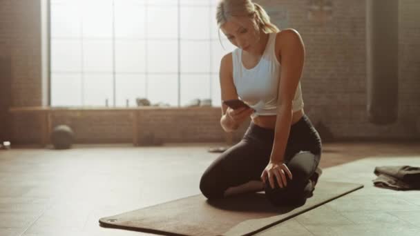 Vacker och ung flicka använder smartphone app till tid hennes träning och börjar göra kör planka på hennes Fitness matta. Gorgeous och atletisk kvinna gör Mountain Climber Workout i snygg Hardcore gym — Stockvideo
