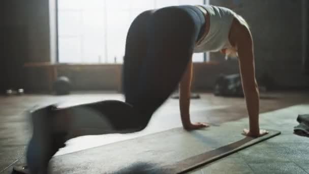Όμορφο και νεαρό κορίτσι χρησιμοποιεί smartphone app για την εγκατάσταση χρονοδιακόπτη για την άσκησή της και αρχίζει να κάνει τρέξιμο σανίδα στο χαλάκι της γυμναστικής. Αθλητική γυναίκα κάνει ορειβατική προπόνηση στο κομψό hardcore γυμναστήριο — Αρχείο Βίντεο