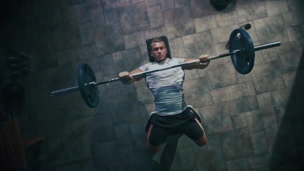Top utsikt över professionell atlet gör bänk press träning med en skivstång i Hardcore gym. Muskulös och atletisk bodybuilder gör barbell övning. Zooma ut — Stockvideo