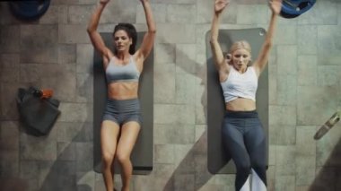 Hardcore Gym Yoga Mats yatarken Iki Profesyonel Kadın Bodybuilders Sit-up Egzersizleri yapıyor. Kas ve Atletik Güzel Kızlar Egzersiz ve Kutlama Yüksek Beş. Üst Görünümü Uzaklaştır