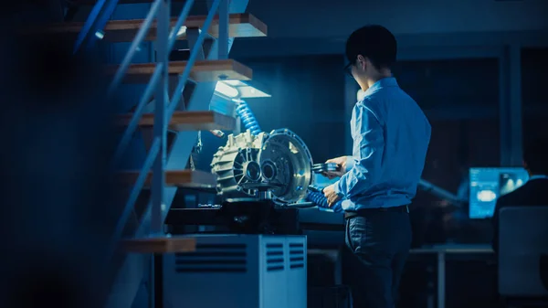 Ingeniero Automotriz Profesional en Gafas está trabajando en engranajes de transmisión en un laboratorio innovador de alta tecnología con pantallas de computadora . — Foto de Stock