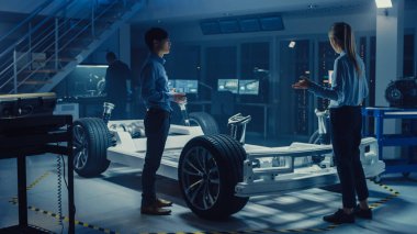 Otomotiv Tasarım Mühendisleri Elektrikli Araç Şasi Prototipi Üzerinde Çalışırken Konuşuyor. Yenilik Laboratuvarı Nda Tesis Konsept Araç Çerçevesi Tekerlekler, Süspansiyon, Motor ve Akü.