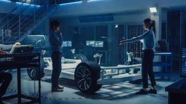 Otomotiv Tasarım Mühendisi ve Tablet ile Bilim Adamı Elektrikli Otomobil Şasi Prototiptartışmak. Yenilik Laboratuvarı Nda Tesis Konsept Araç Çerçevesi Tekerlekler, Süspansiyon, Motor ve Akü