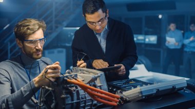 Tablet Bilgisayar ve Denetim Araçları ile İki Profesyonel Otomotiv Mühendisleri Bir Konsept Otomobil Şasi ile Yüksek Teknoloji Laboratuvarında Bir Elektrik Motoru Test Ederken Bir Konuşma Yapıyor.