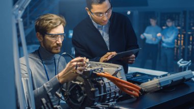 Tablet Bilgisayar ve Denetim Araçları ile İki Profesyonel Otomotiv Mühendisleri Bir Konsept Otomobil Şasi ile Yüksek Teknoloji Laboratuvarında Bir Elektrik Motoru Test Ederken Bir Konuşma Yapıyor.