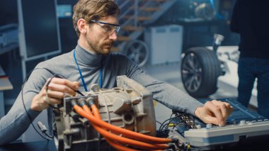 Bilgisayar ve Denetim Araçları ile Gözlük Profesyonel Otomotiv Mühendisi Bir Konsept Otomobil Şasi ile Yüksek Teknoloji Laboratuvarında Kullanılmış Elektrikli Motor Test.