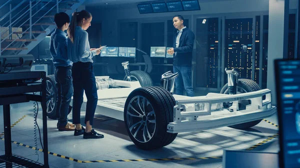 전기 자동차 섀시 프로토타입을 작업하는 동안 자동차 설계 엔지니어가 이야기하고 있습니다. 혁신 실험실 시설 개념 차량 프레임에는 바퀴, 서스펜션, 엔진 및 배터리가 포함됩니다.. — 스톡 사진