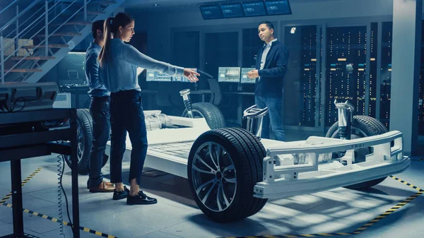 Ingénieurs de conception automobile parler tout en travaillant sur le prototype de châssis de voiture électrique. Dans le concept d'installation de laboratoire d'innovation, le cadre du véhicule comprend les roues, la suspension, le moteur et la batterie . — Photo