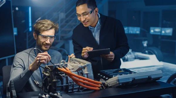 Dois engenheiros automotivos profissionais com um computador tablet e ferramentas de inspeção estão tendo uma conversa enquanto testam um motor elétrico em um laboratório de alta tecnologia com um chassi de carro conceito . — Fotografia de Stock