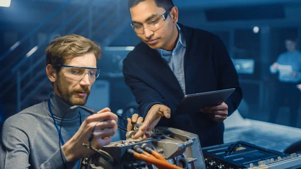 Dos ingenieros automotrices profesionales con una tableta y herramientas de inspección están teniendo una conversación mientras prueban un motor eléctrico en un laboratorio de alta tecnología con un chasis de automóvil conceptual . — Foto de Stock