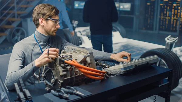 Профессиональный автомобильный инженер в очках с компьютерными и инспекционными инструментами тестирует подержанный электромотор в лаборатории высоких технологий с концептуальным автомобильным шасси . — стоковое фото