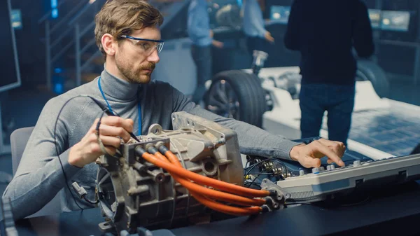 Profesjonalny inżynier samochodowy w okularach z komputerem i narzędziami inspekcyjnych testuje używany silnik elektryczny w High Tech Laboratory z koncepcyjnym podwoziem samochodowym. — Zdjęcie stockowe