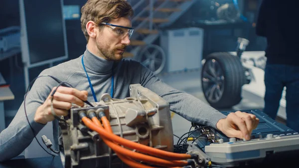 Engenheiro automotivo profissional em óculos com um computador e ferramentas de inspeção está testando um motor elétrico usado em um laboratório de alta tecnologia com um chassi de carro conceito . — Fotografia de Stock