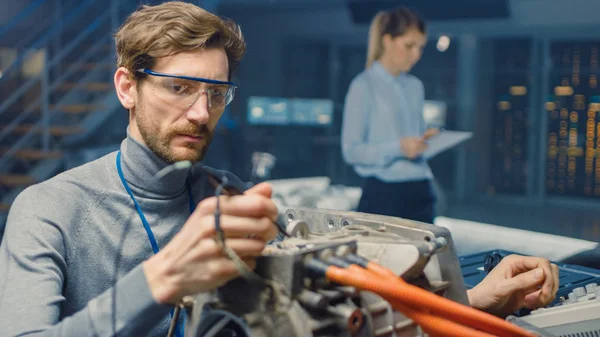 Ingénieur automobile professionnel en lunettes avec un ordinateur et des outils d'inspection teste un moteur électrique usagé dans un laboratoire de haute technologie avec un châssis Concept Car . — Photo