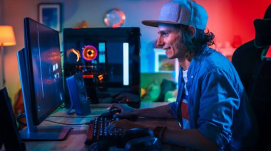 Renkli Neon Led Işıklar ile Onun Güçlü Kişisel Bilgisayar first-person Shooter Online Video Oyunu Oynarken Profesyonel Gamer. Genç Adam Şapka Takıyor. Oturma Odası Sıcak Kırmızı Lambalar ile Aydınlatılmış. Akşam.