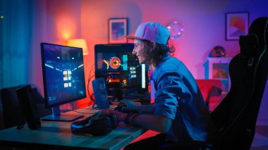 Renkli Neon Led Işıklar ile Onun Güçlü Kişisel Bilgisayar first-person Shooter Online Video Oyunu Oynarken Profesyonel Gamer. Genç Adam Şapka Takıyor. Oturma Odası Sıcak Kırmızı Lambalar ile Aydınlatılmış. Akşam.