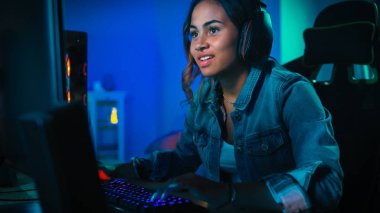 Kulaklık Pretty ve Heyecanlı Black Gamer Girl Onun Bilgisayarda First-Person Shooter Online Video Oyunu Oynuyor. Oda ve Pc Renkli Neon Led Işıklar var. Evde Rahat Akşam.