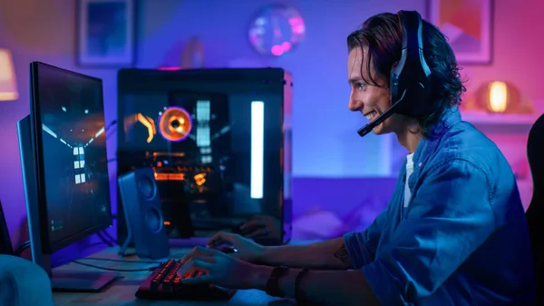 Upphetsad Gamer spelar första-person shooter online video spel på sin persondator. Rummet och datorn har färgglada Neonled-lampor. Ung man har långt hår. Mysig kväll hemma. — Stockfoto