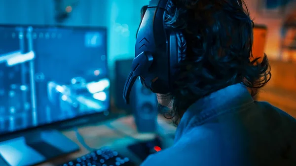 Nahaufnahme eines Spielers, der ein Headset mit Mikrofon trägt und auf seinem PC ein Online-Shooter-Videospiel spielt. Zimmer und PC haben bunte Neon-LED-Lichter. Gemütlicher Abend zu Hause. — Stockfoto