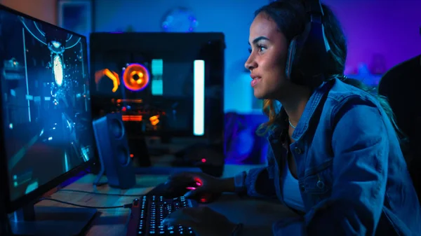 Szép és izgatott fekete Gamer lány fejhallgató játszik First-person shooter online video játék a számítógépe. Szoba és PC színes neon LED fények. Meghitt este otthon. — Stock Fotó