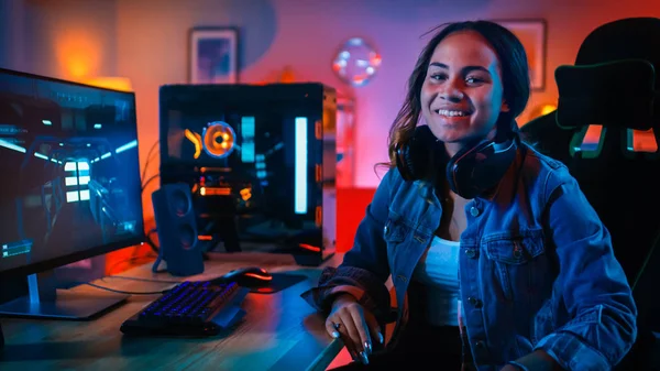 Retrato de uma garota Gamer bonita e excitada em fones de ouvido que terminou de jogar videogame em seu computador. Ela se vira e sorri para a câmera. Casa é Lit com luzes de néon . — Fotografia de Stock