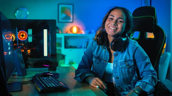 Ritratto di una bella ed eccitata ragazza nera Gamer in cuffie che ha finito di giocare al videogioco sul suo computer. Si trasforma e sorride nella macchina fotografica. Casa è accesa con luci al neon . — Foto Stock