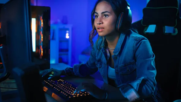 Ładne i podekscytowany Black Gamer Dziewczyna w słuchawkach jest zestresowany gra strzelanka z perspektywy pierwszej osoby online gry wideo na jej komputerze. Pokój i komputer mają kolorowe Neon LED Lights. Przytulny wieczór w domu. — Zdjęcie stockowe